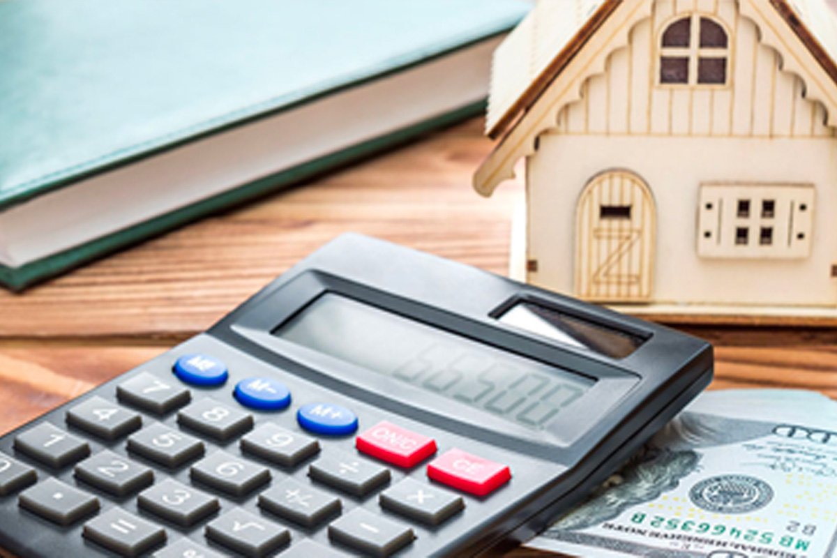 calculator, money and a small wooden house on a table