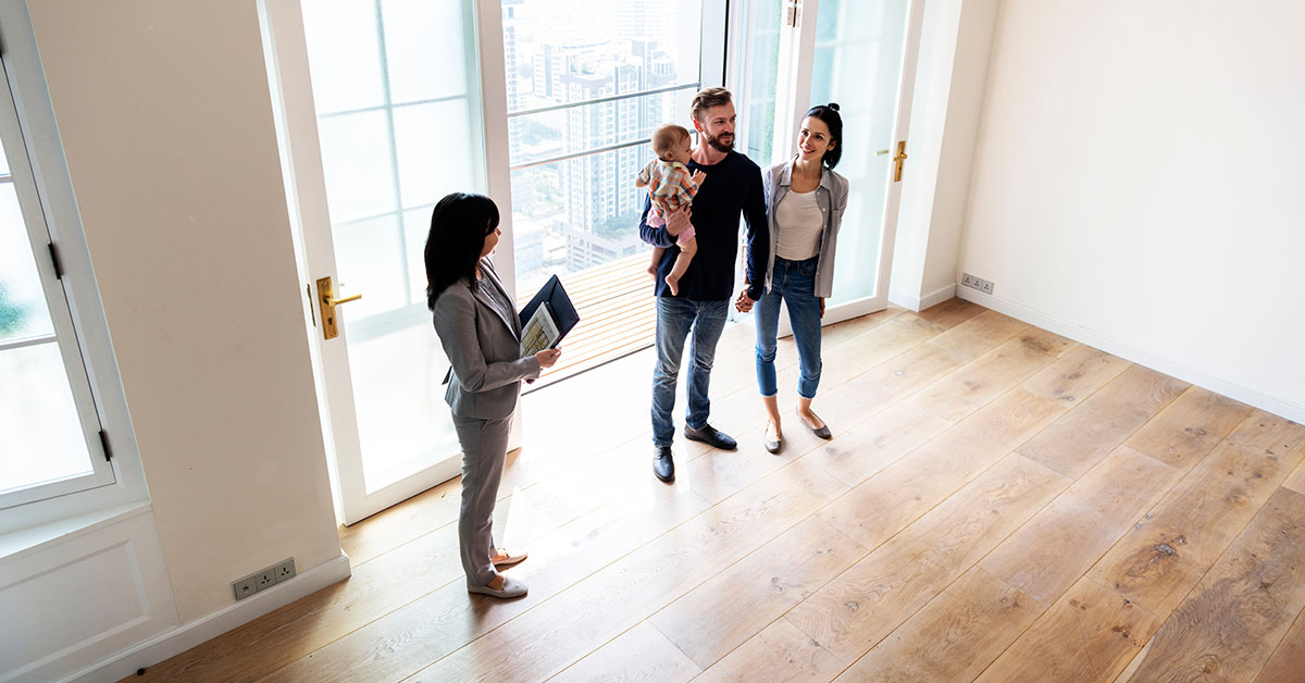 Family of three stands in the living room of a house they are viewing with a realtor.