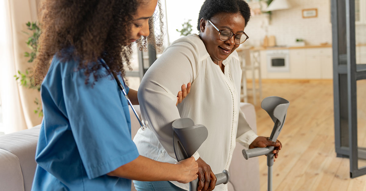 A nurse helps a woman use crutches in her home