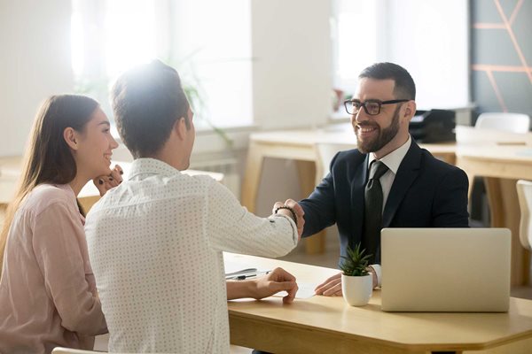 Man and woman sitting across from a man in a business suit, shaking hands