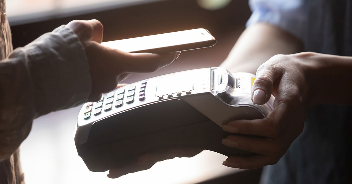 A person holds a payment processing machine while another person holds up a phone to the machine for a touchless payment transaction.