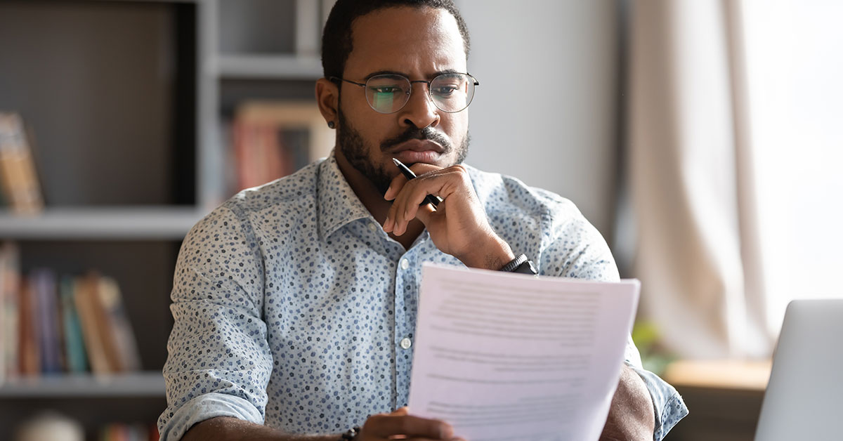 Man holding tax forms sitting at a desk in front of a laptop