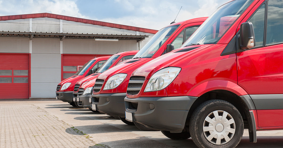 Row of red company delivery vans sitting outside a warehouse.