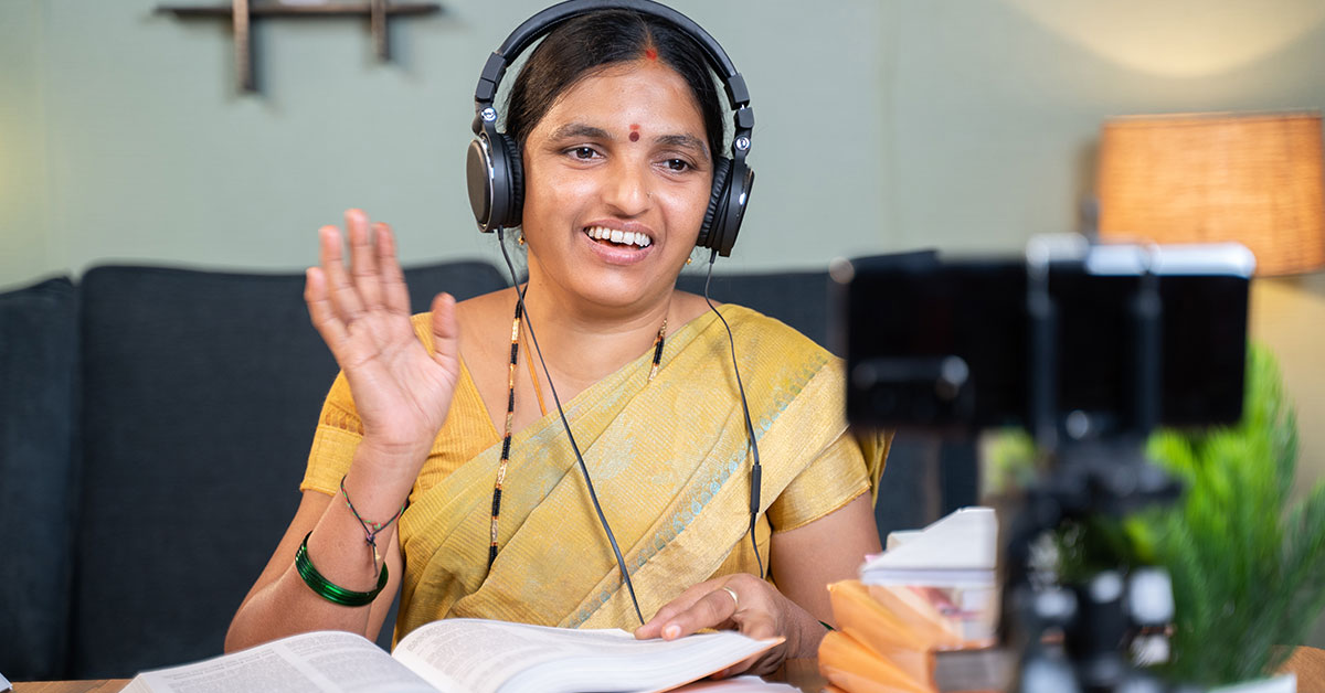 A woman wears headphones and speaks to the camera as she records a language lesson.