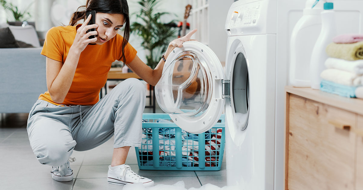 Frustrated woman calls a repair service while inspecting her broken washing machine.