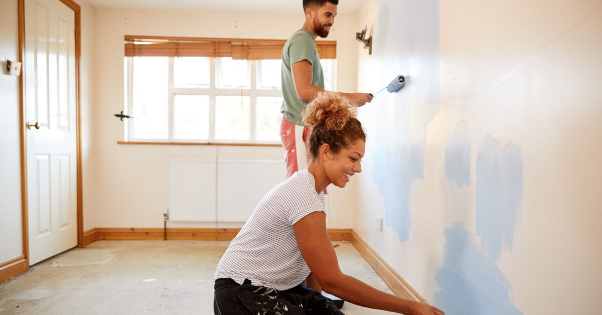 Couple smiles as they paint a room in their new home.