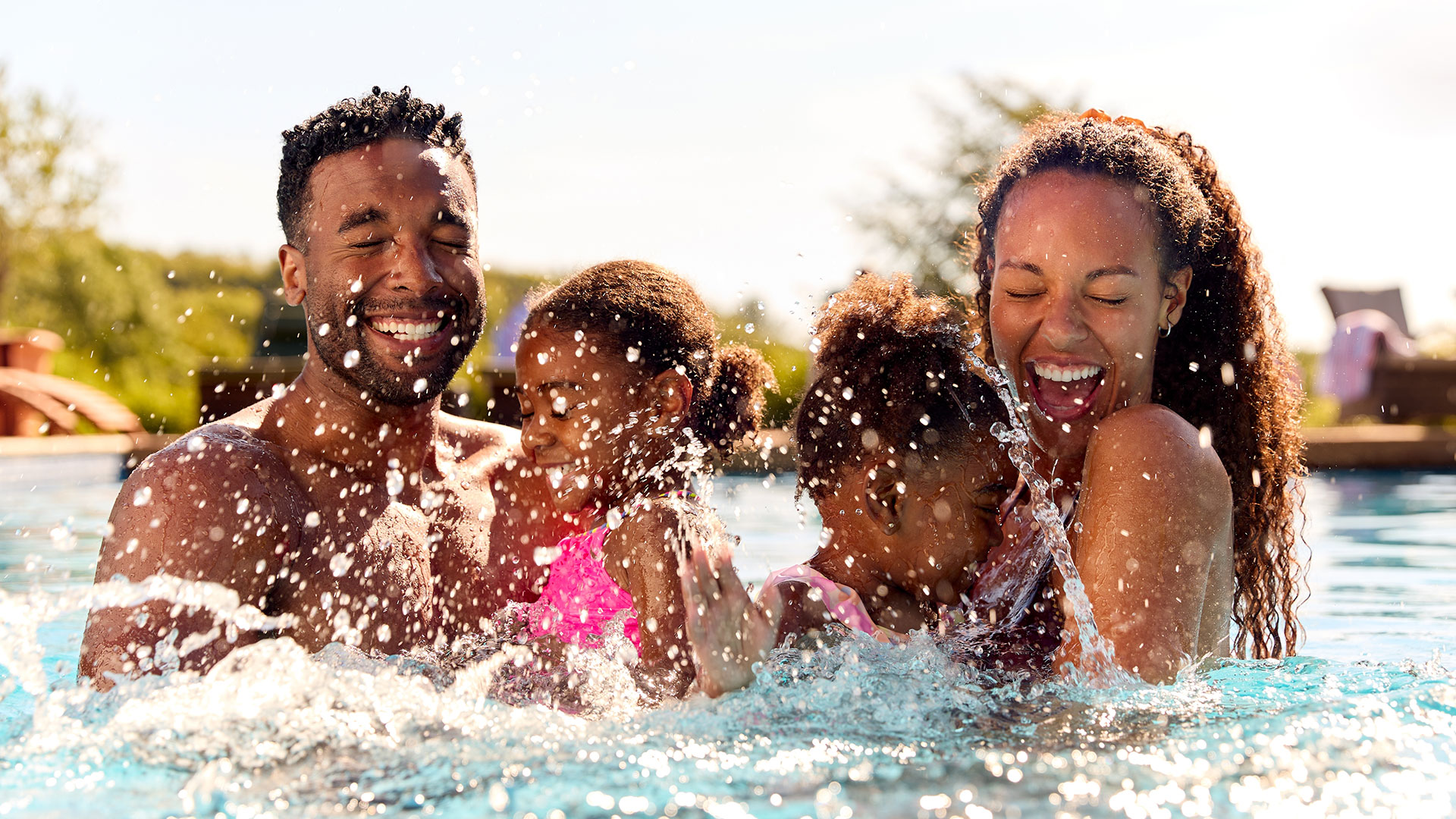 Family of four laughs as they splash in the pool on vacation.