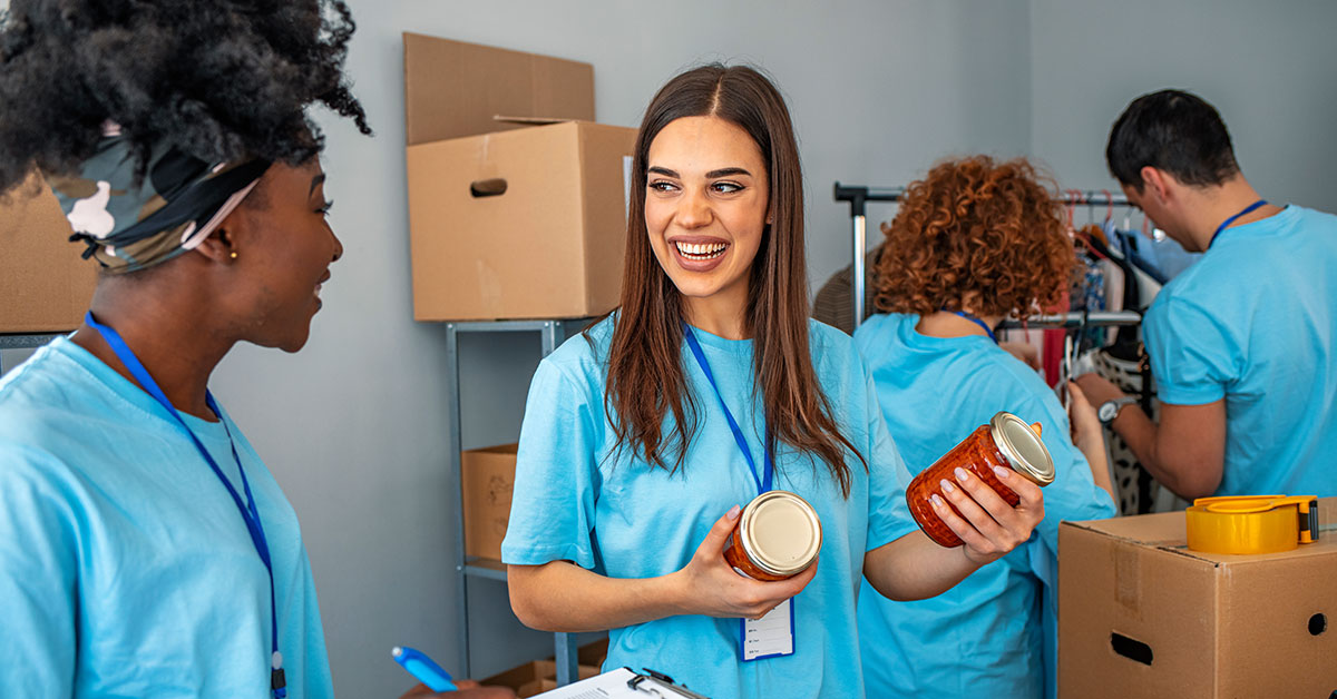 Two volunteers smile as they sort canned goods for a donation drive.