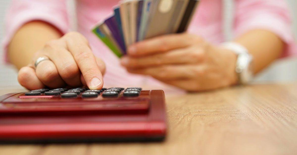 Woman types on a calculator while holding several credit cards.