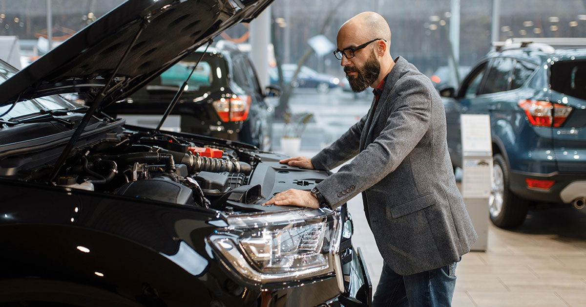 Man standing in automobile show room looking under the hood of a large SUV he wants to buy