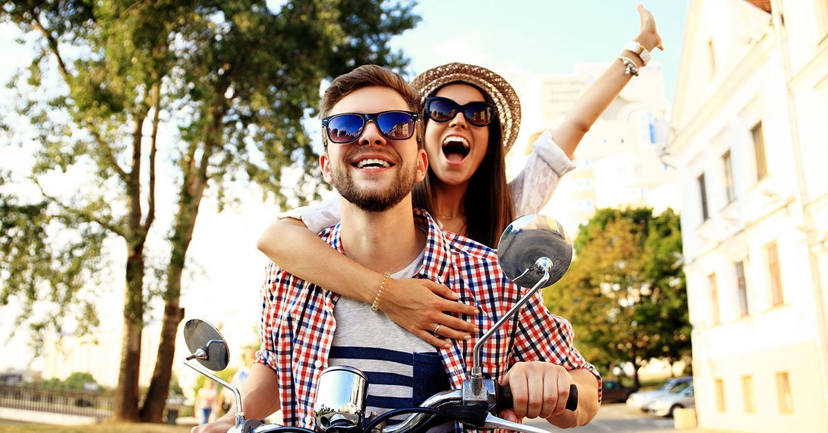 Couple on motorbike smiles as they zoom down a road towards the camera