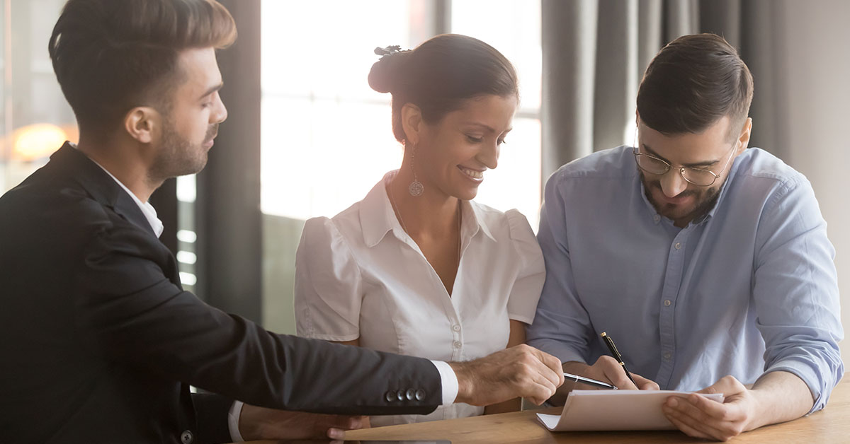 Happy couple fills out car financing paperwork with their banker