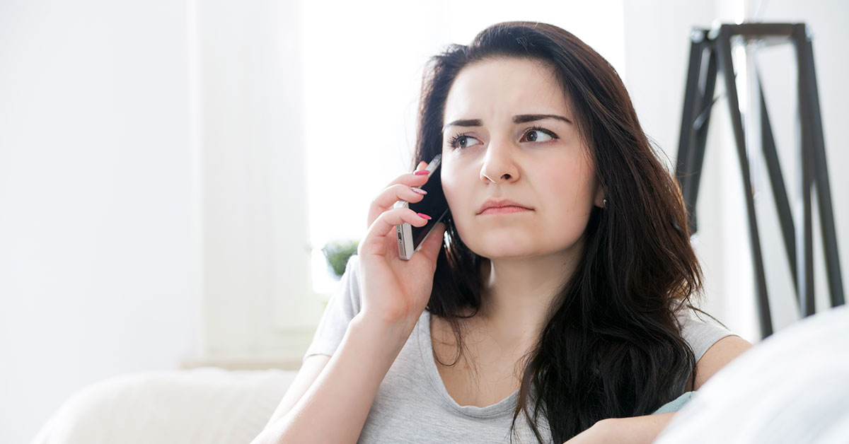Photo of a young woman sitting on a couch. She is on her cell phone and has a concerned expression