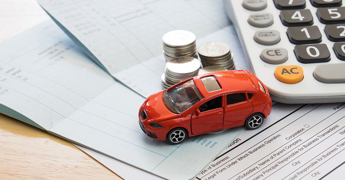Photo of a red toy car, stack of coins and calculator all sitting on top of a check book ledger and car loan application.