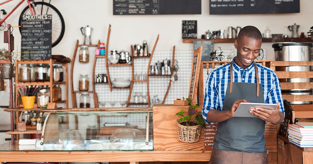 smiling business owner looking at a tablet while in front of the counter