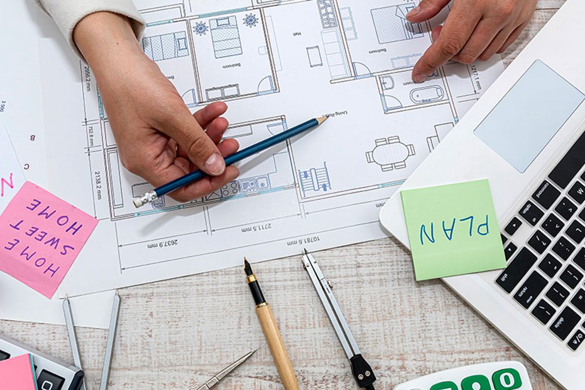 A hand with a blue pencil, pointing to an architectural plan.