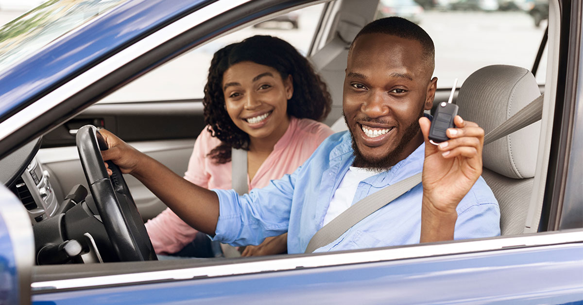 View inside open automobile driver’s side window of a smiling young man and woman who just purchased their new car with an auto loan express draft