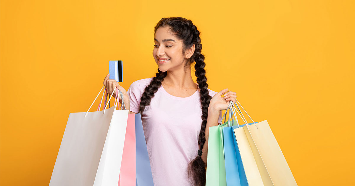 Woman smiles down at her credit card in one hand while holding several shopping bags with purchases she made with her credit card rewards points.