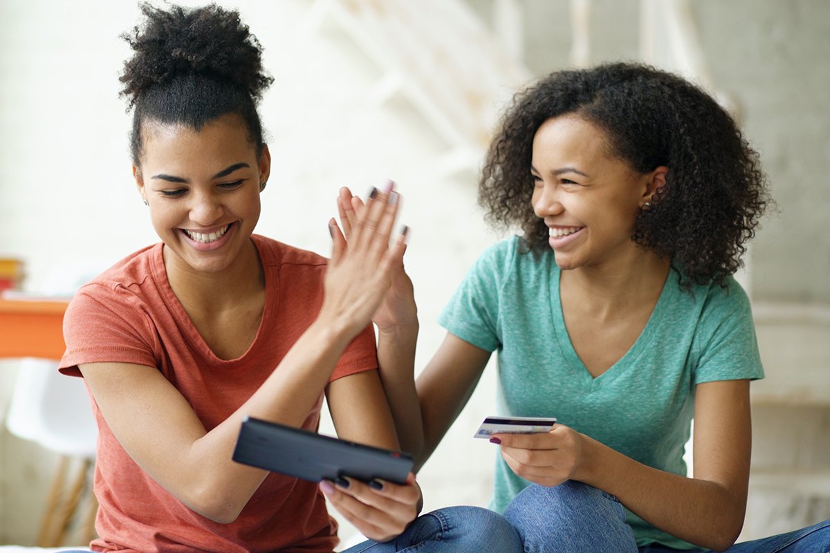 two women high-fiving while one holds a credit card