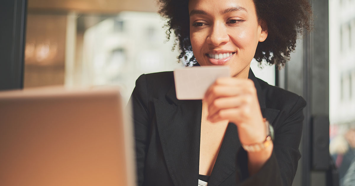 Smiling woman uses her credit card to online shop on her laptop