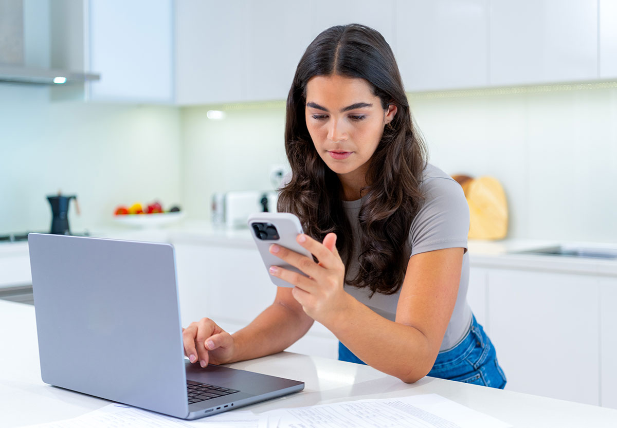 Woman Looking at Her Mobile Phone with Laptop