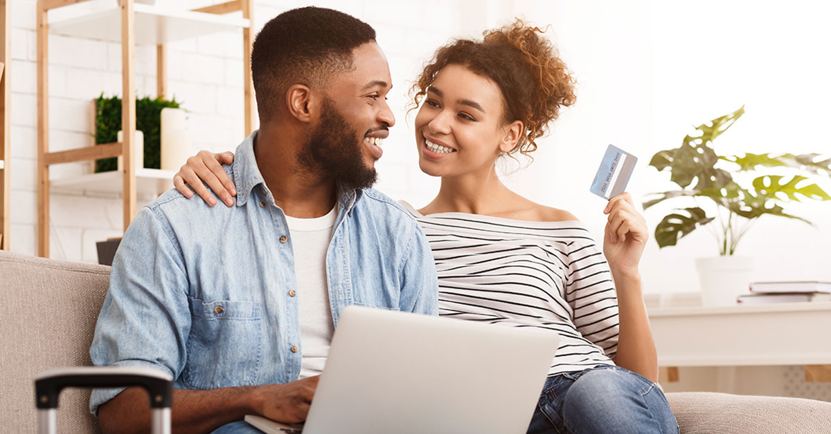 Photograph of a couple seated on a couch, with woman holding her credit union credit card in air as they are discussing a joint purchase