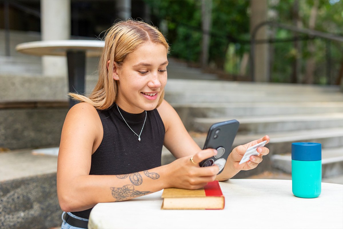 college student at a table holding a phone and a credit card