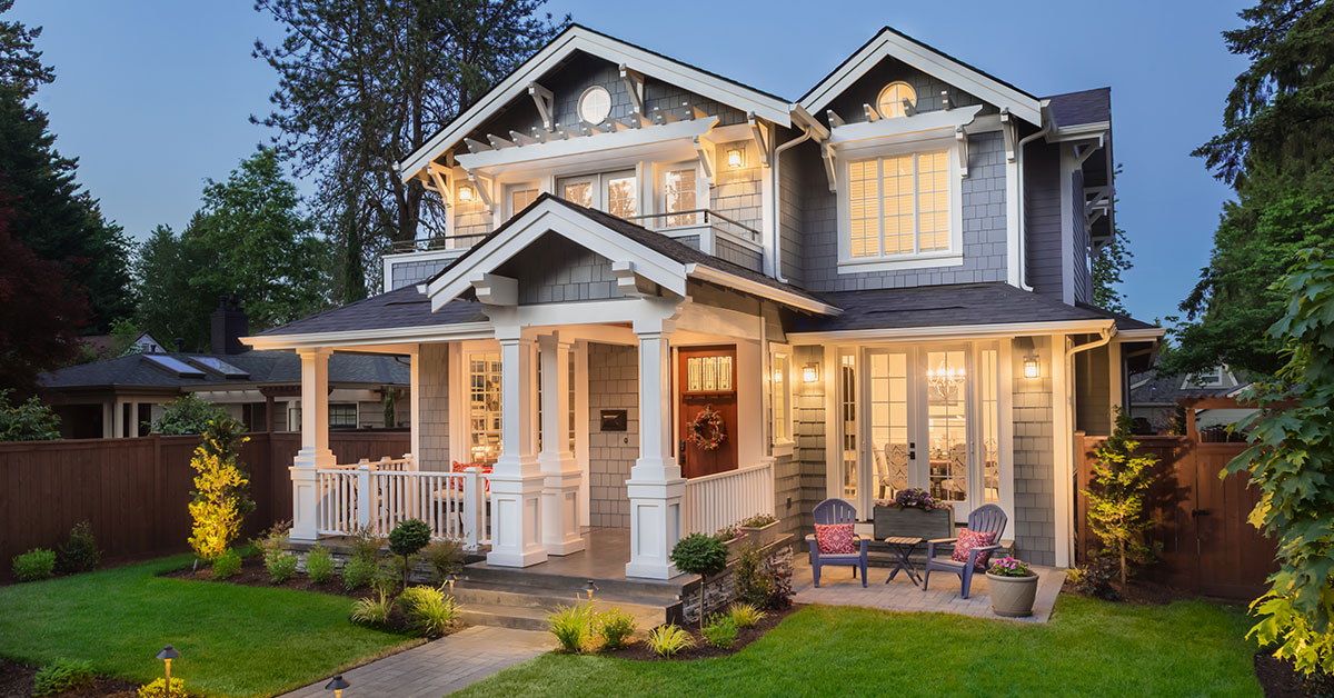 A two-story, light blue home with white trim and a small, well-manicured lawn at dusk.