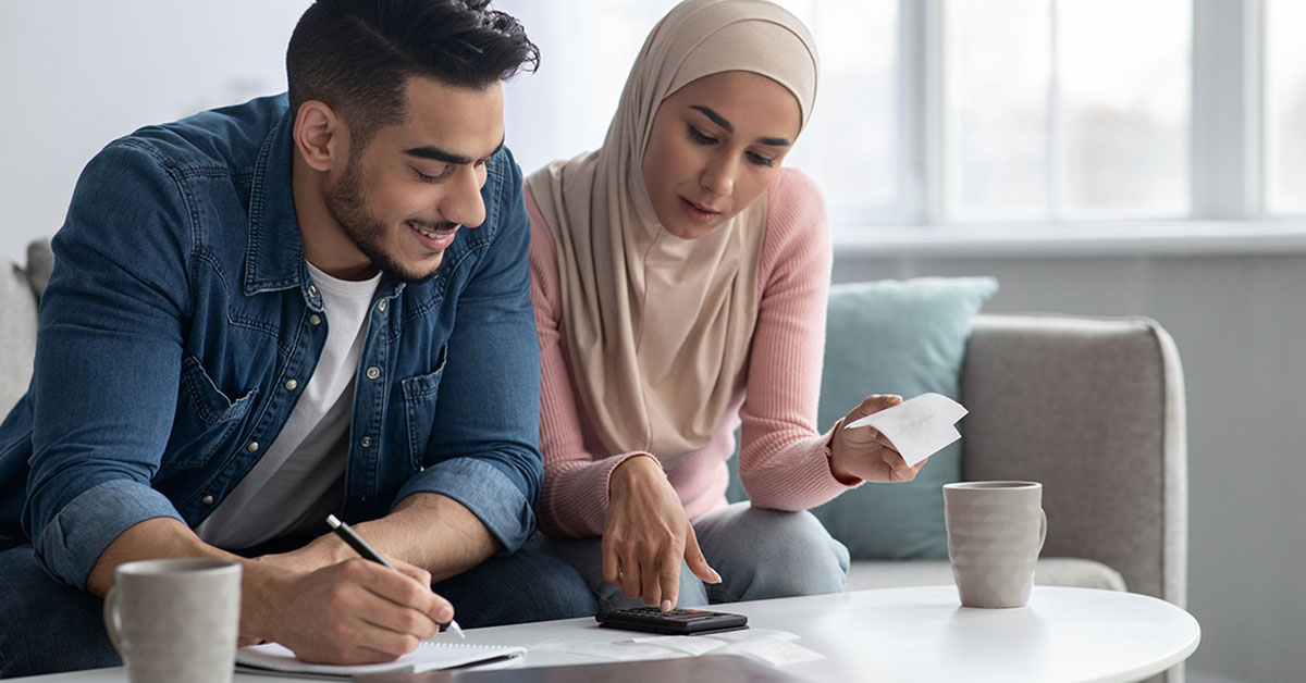 Husband and wife sitting on the couch with a laptop and calculator creating a plan for their monthly budget