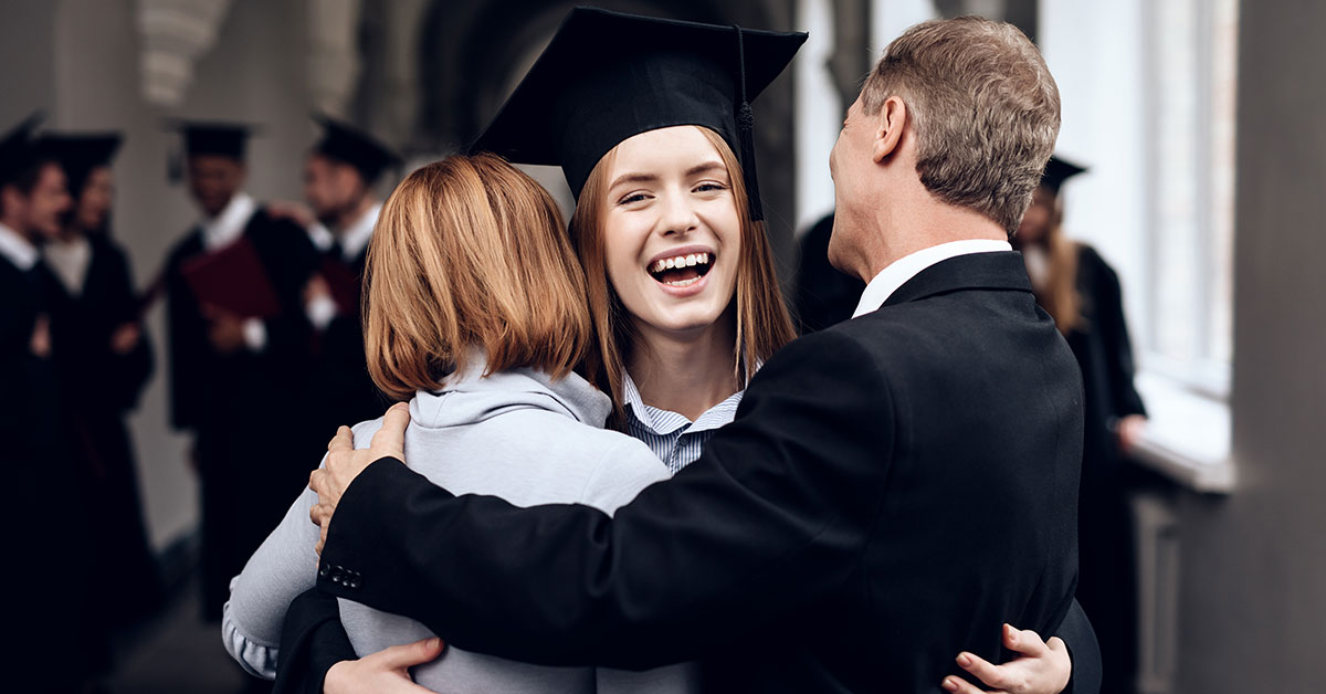 Young woman hugging her family at her college graduation