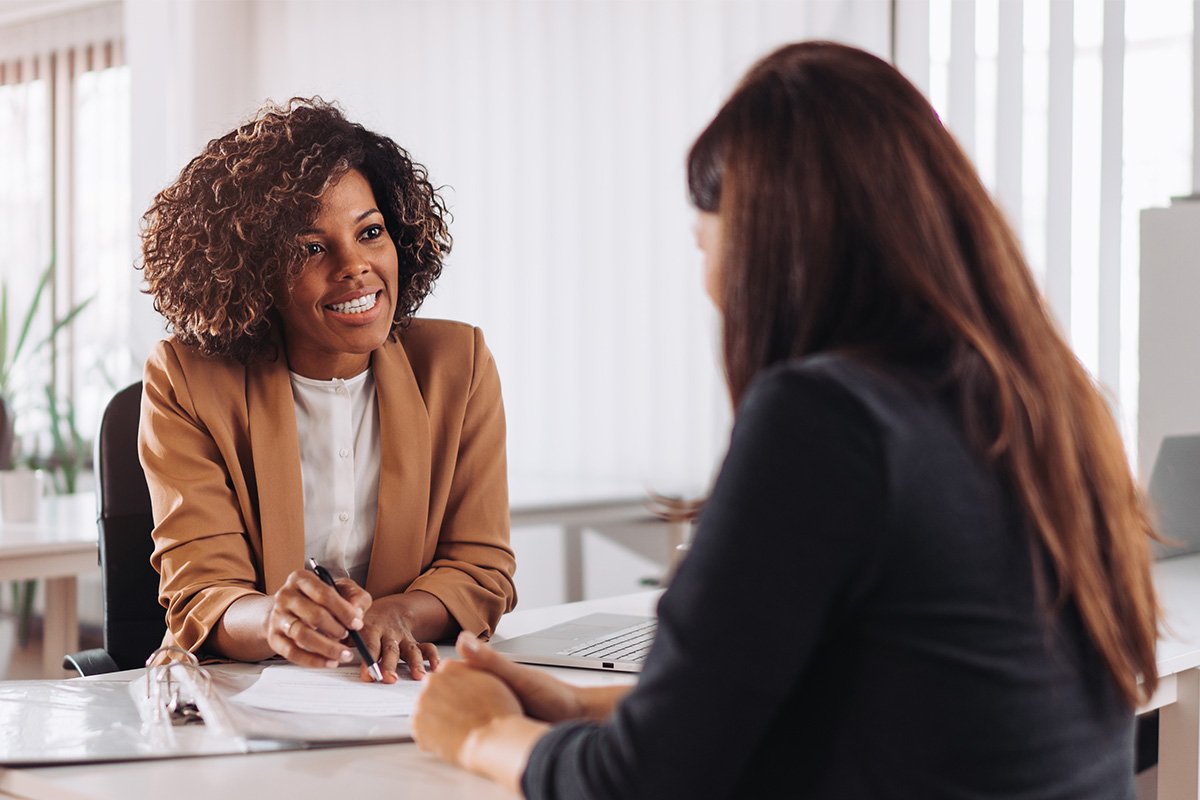 Business women pointing at paperwork with women at desk.