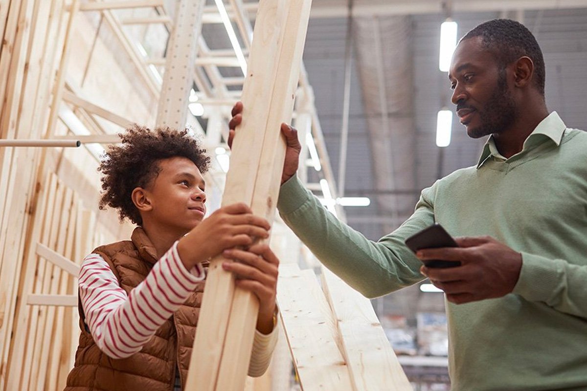 A father and son holding up a wooden beam for a house