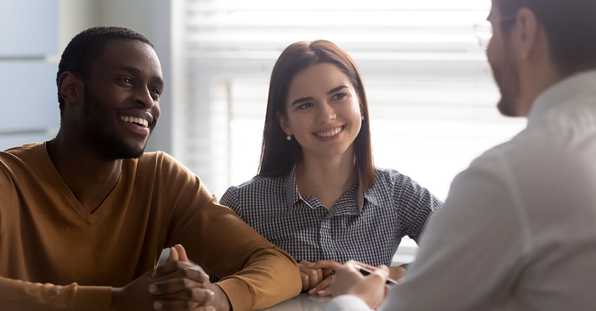 A young couple smiles as they talk with a credit union employee.