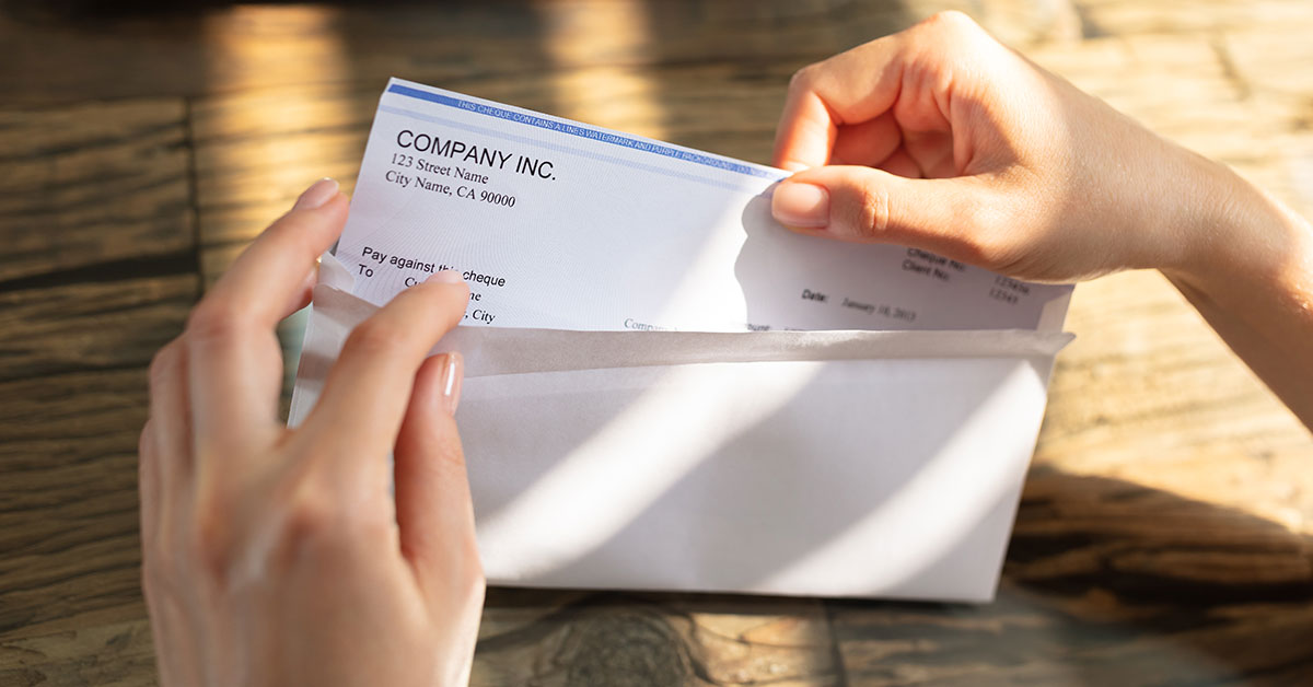 Close up of a woman’s hands opening an envelope and pulling out a paycheck