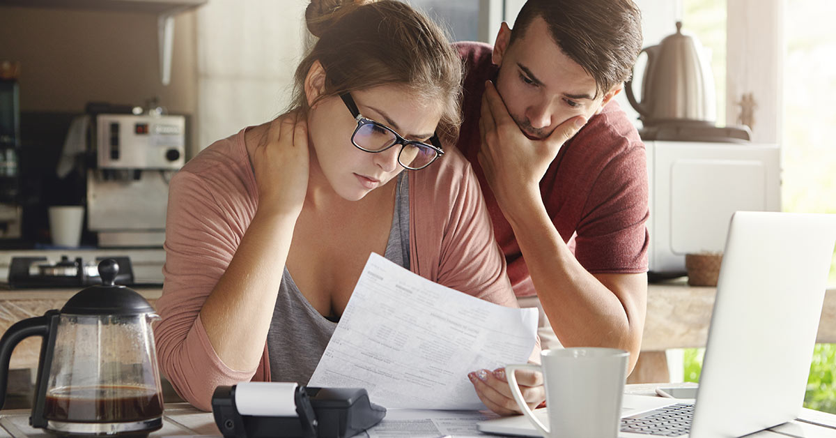 A young couple standing in their kitchen, attentively looking at a piece of mail together.