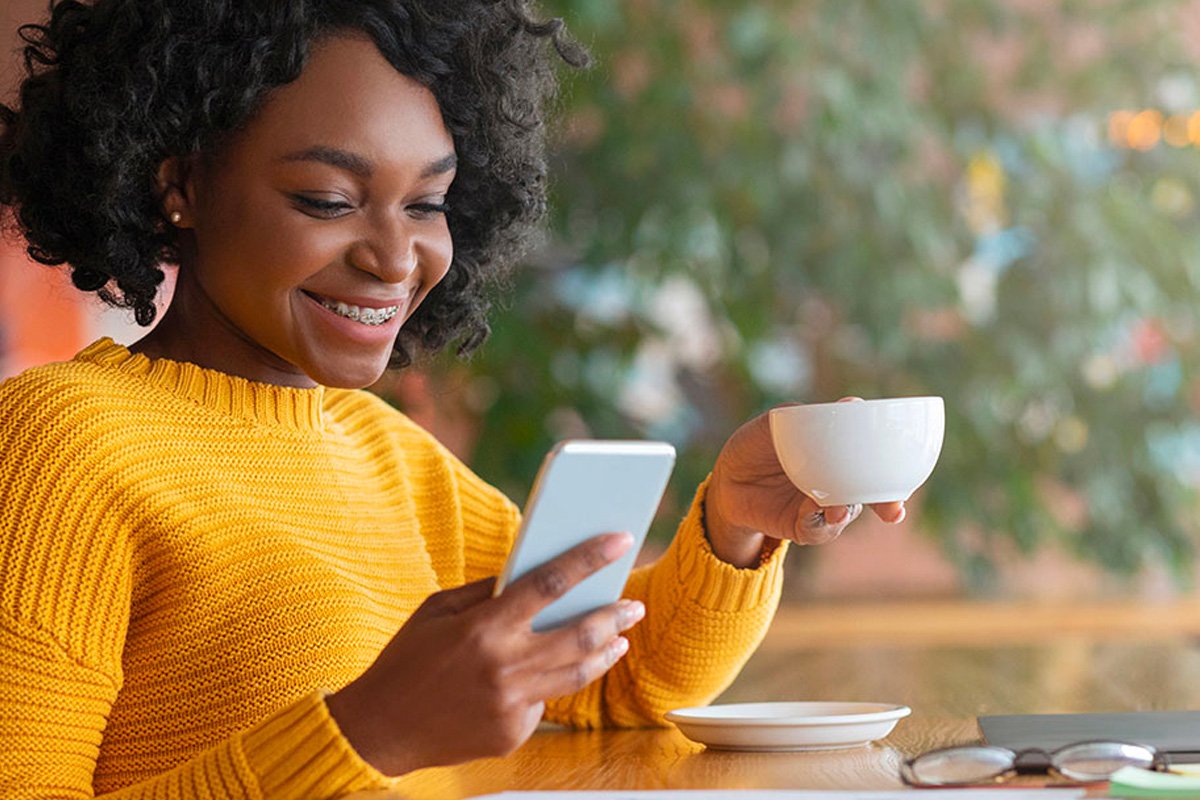 A woman holding a cup looking at her smartphone.