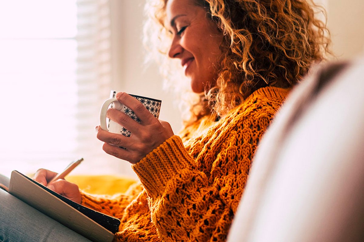 woman writing and drinking a beverage