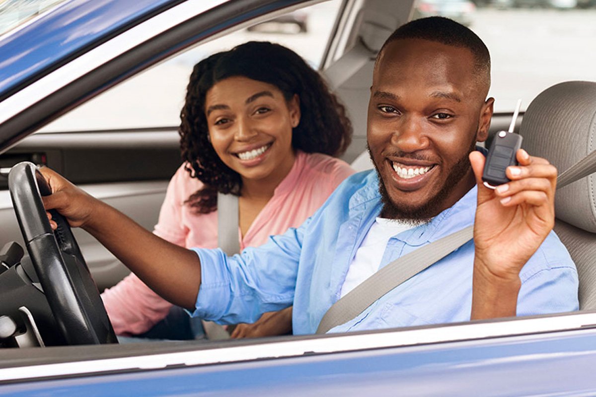 A smiling couple sitting inside their new car, receiving the keys.