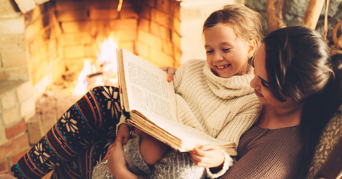 Young mother reading a Christmas story with her daughter by the fireplace