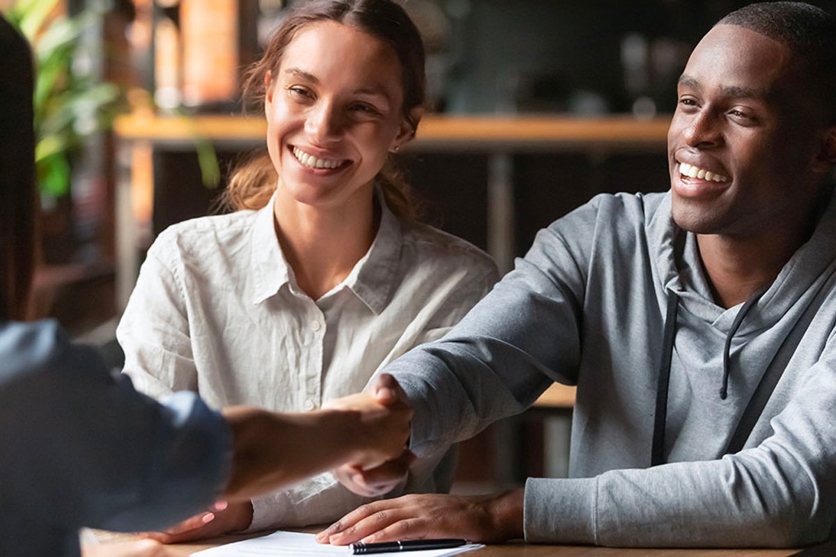 A girl and a boy closing a contract with an agent, shaking hands.