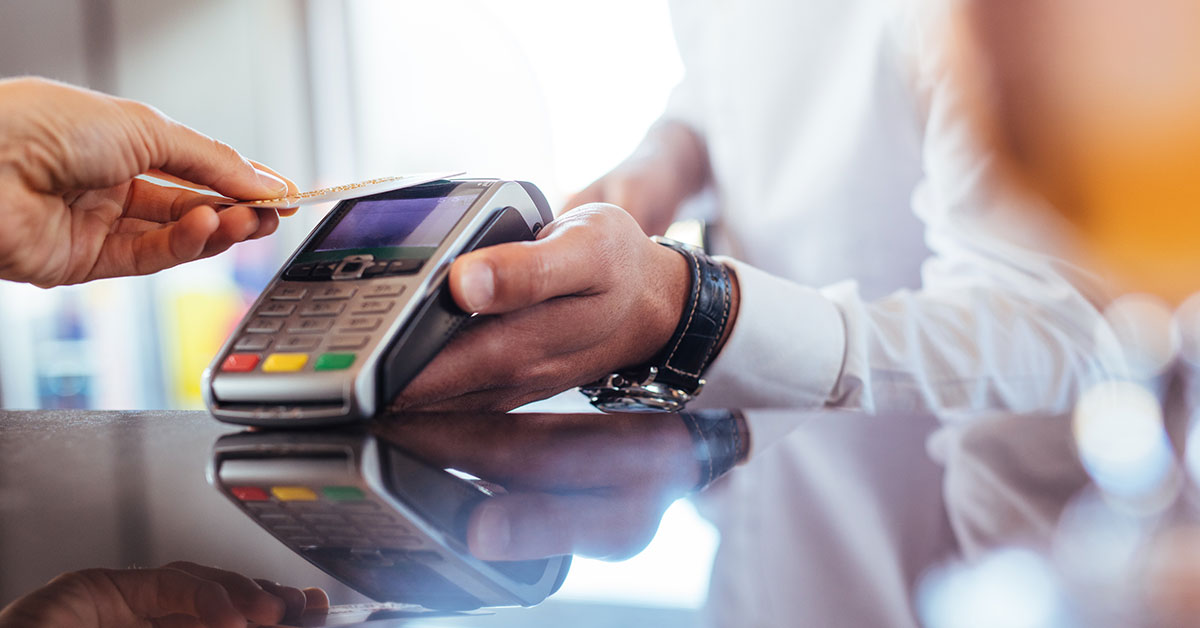 Person taps a credit card on a Point of Sale device to pay for a transaction.