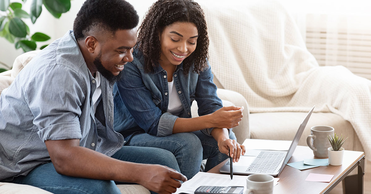 Excited young couple seated together on couch in apartment budgeting for their future