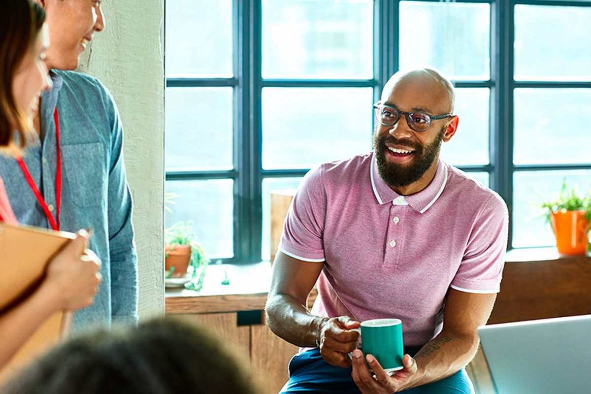 Man holding a cup in his hands and conversing with other people