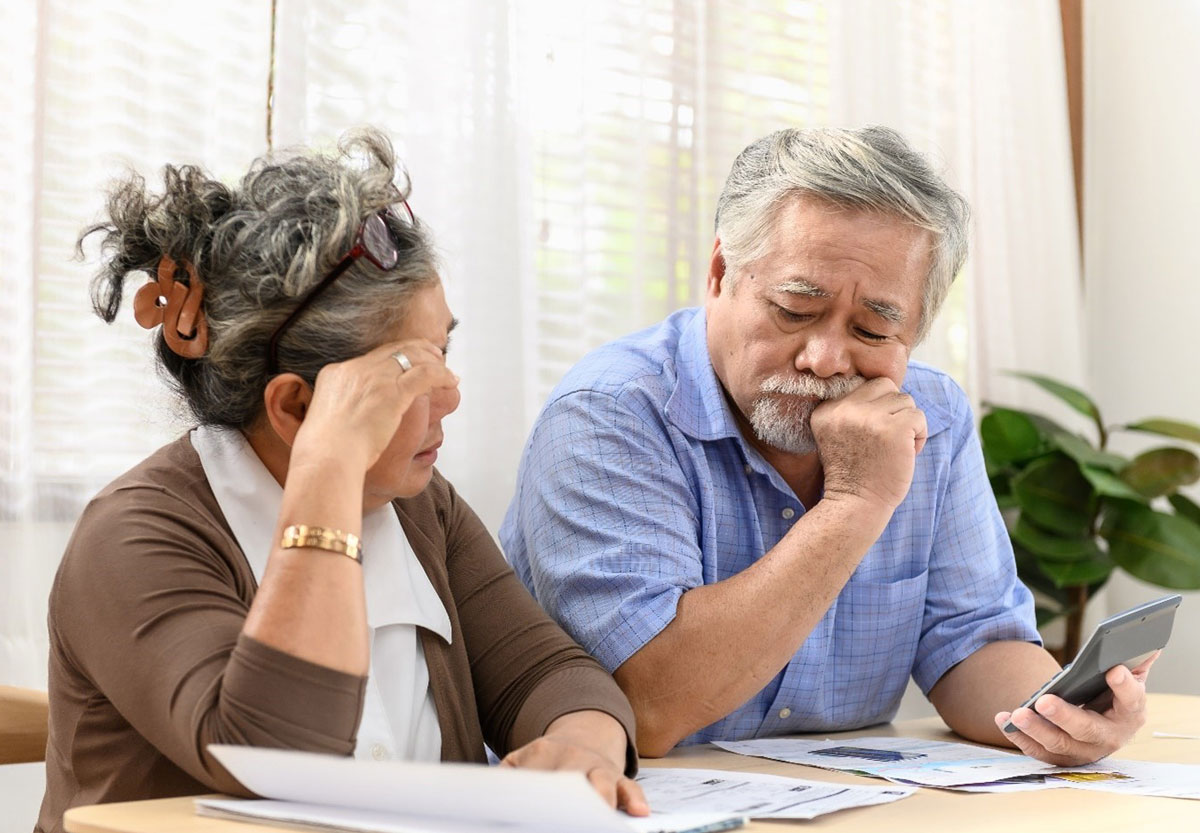 Senior couple sitting at table with multiple bills and a calculator looking concerned