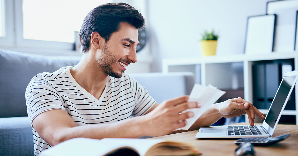 Young happy man reviews his bills and credit history on his laptop